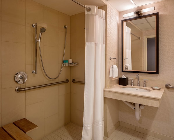 Une salle de bain équipée d’une douche, de barres d’appui, d’un lavabo et d’un miroir.