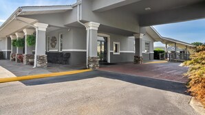 Una entrada de hotel con asientos al aire libre techados, pilares de piedra y un camino pavimentado.
