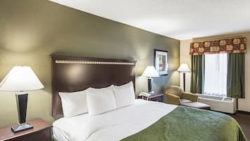 A hotel room with a large bed, two bedside lamps, a chair, a desk with a telephone, and a window with curtains.