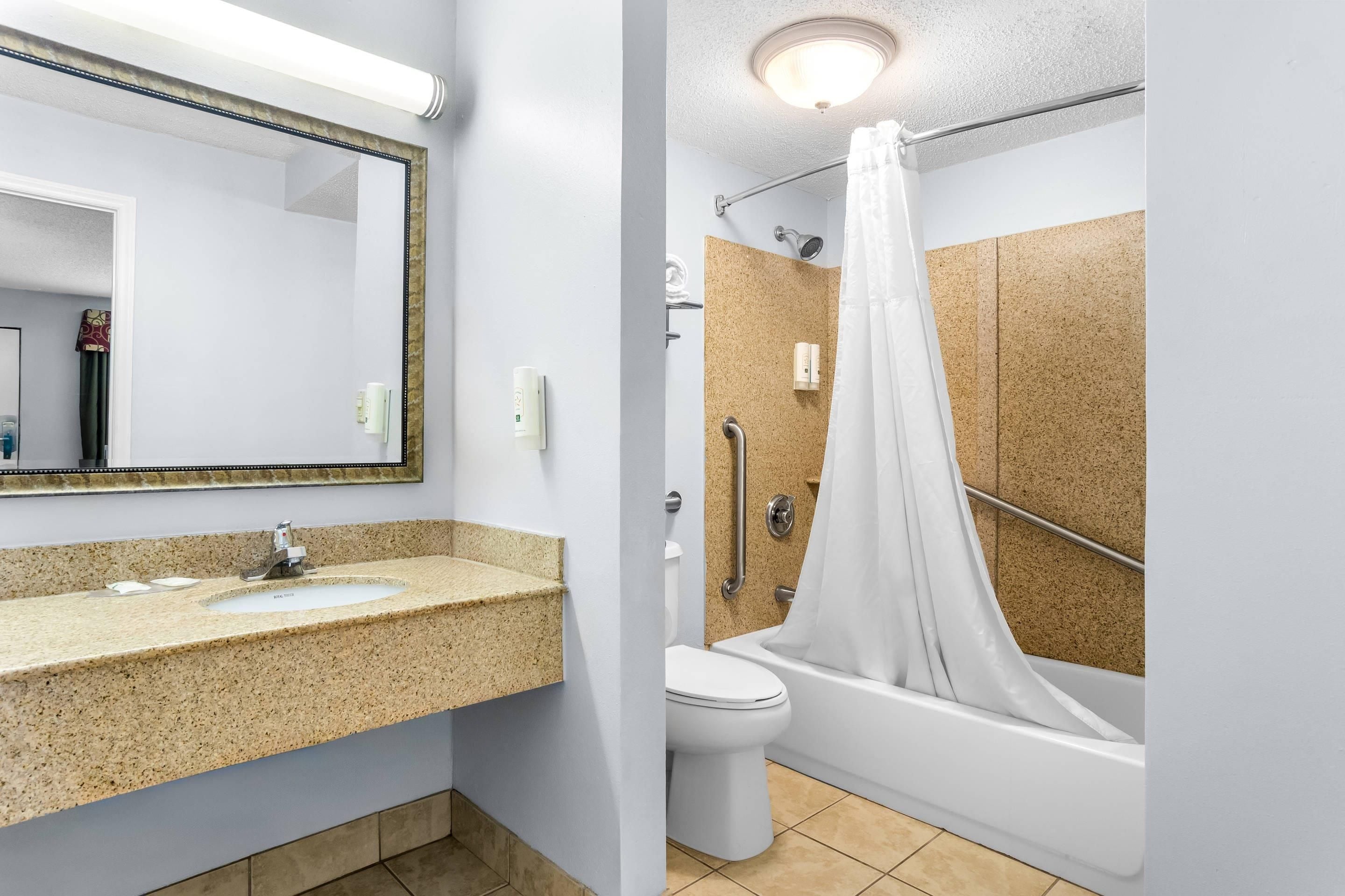 A bathroom with a granite countertop sink, a white toilet, and a bathtub with a shower curtain.