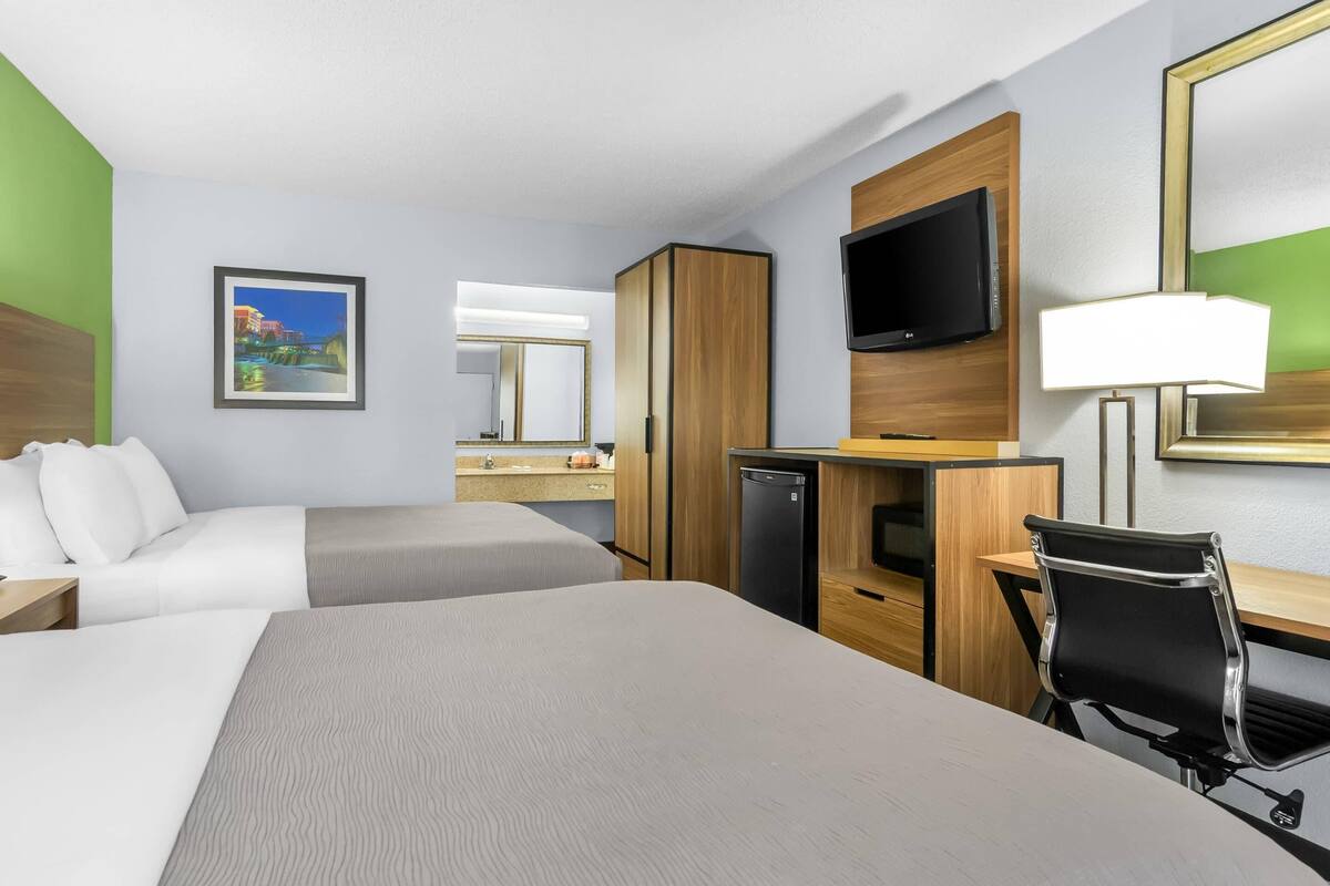 A hotel room with two beds, a desk, a chair, a television, a mirror, and a picture on the wall.