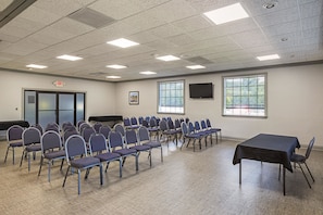 A conference room with rows of chairs, a table, a projector screen, and windows. - Quality Inn & Suites Greenville - Haywood Mall (Greenville)