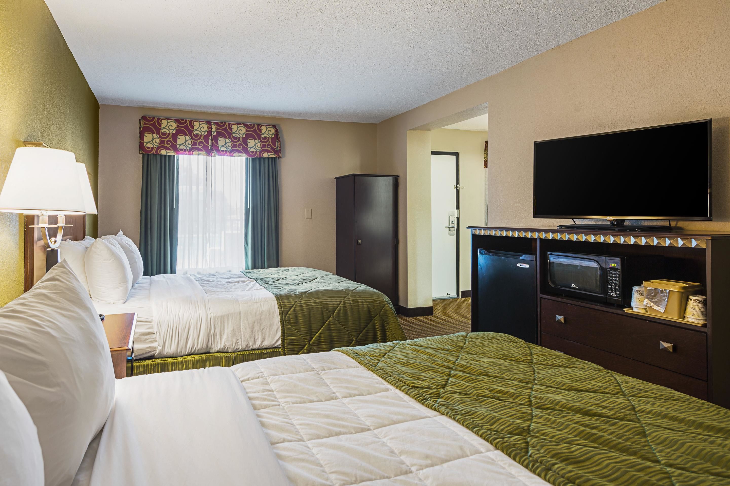 A hotel room with two beds, a television, a microwave, and a cabinet.