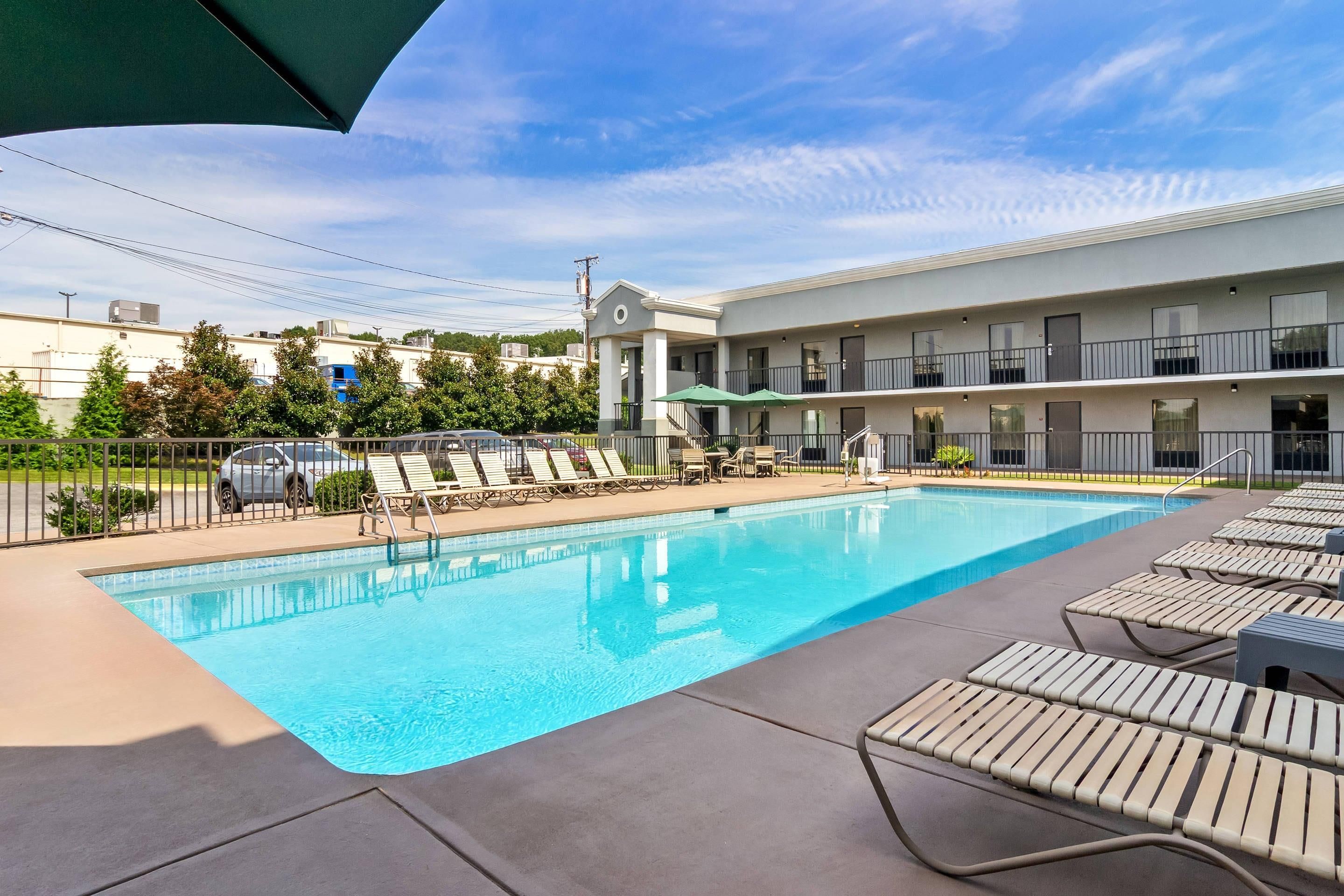 A swimming pool with lounge chairs, a covered area, and a building with balconies in the background.