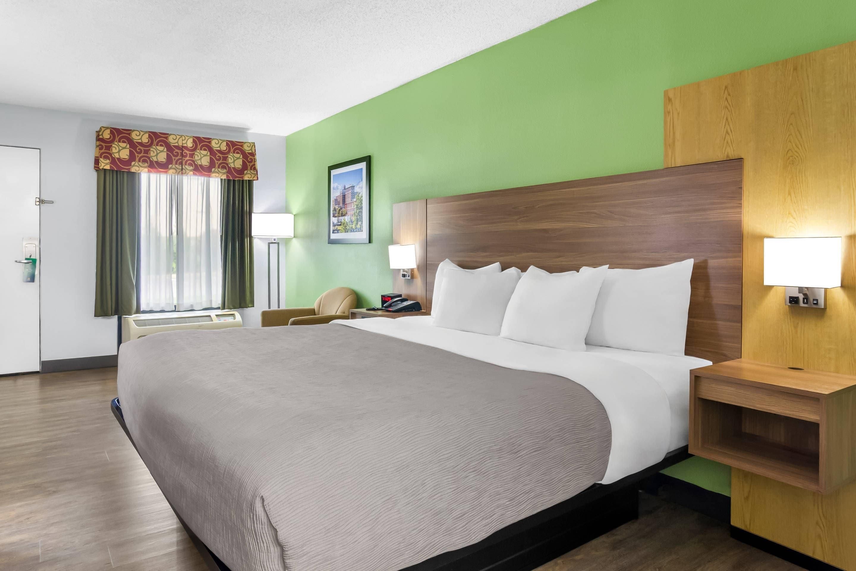 A hotel room with a large bed, green walls, and a wooden headboard.