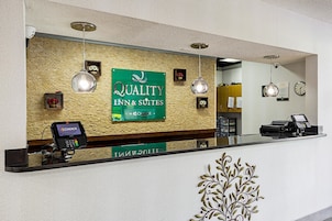 Zona de recepción con un letrero de Quality Inn & Suites, un mostrador de recepción, una caja registradora y una cámara de seguridad.