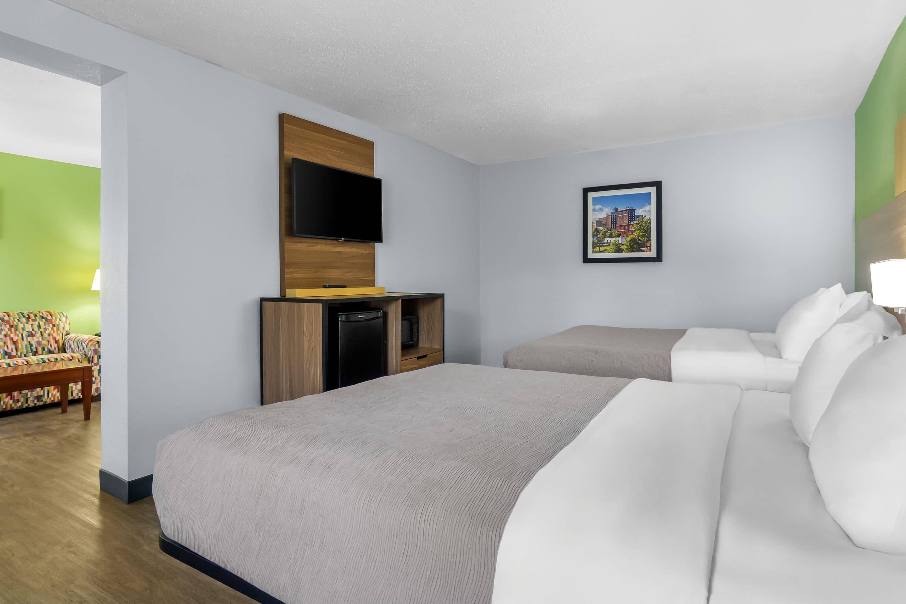 A hotel room with a large bed, a sofa, a flat-screen TV mounted on a wooden panel, a small desk with a computer, and a framed picture on the wall.