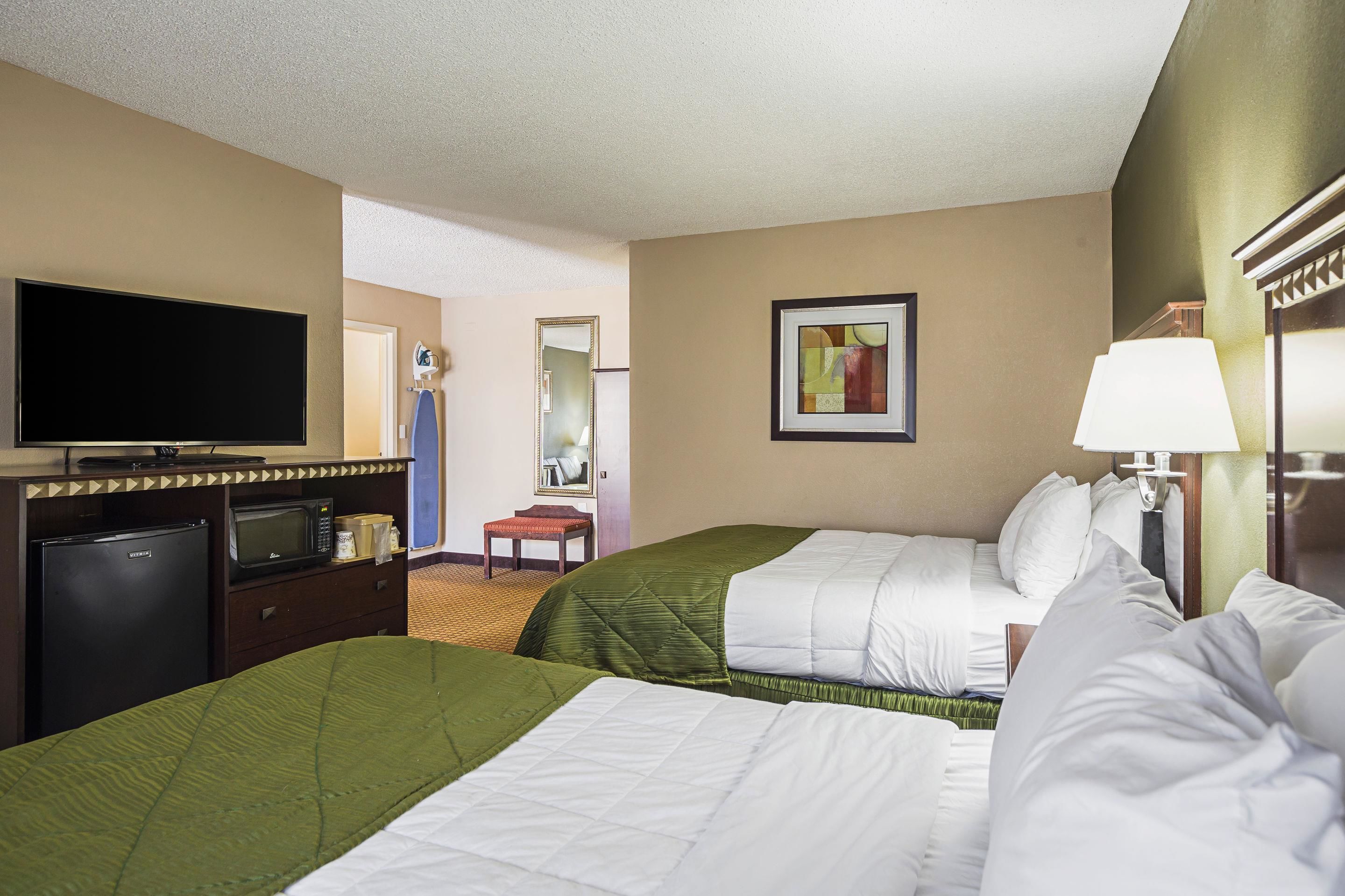 A hotel room with two beds, a television, a microwave, and a desk.