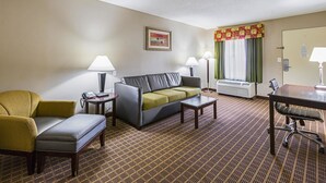 A hotel room with a sofa, armchair, and a small table. There is a window with curtains and a door. - Quality Inn & Suites Greenville - Haywood Mall (Greenville)