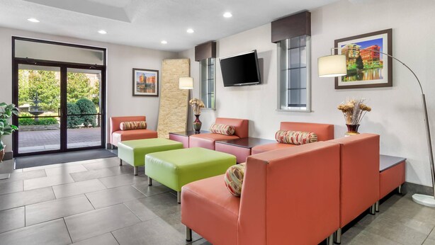 A modern lobby with orange and green seating, a flat-screen TV, and a large window offering a view of greenery. - Quality Inn & Suites Greenville - Haywood Mall (Greenville)