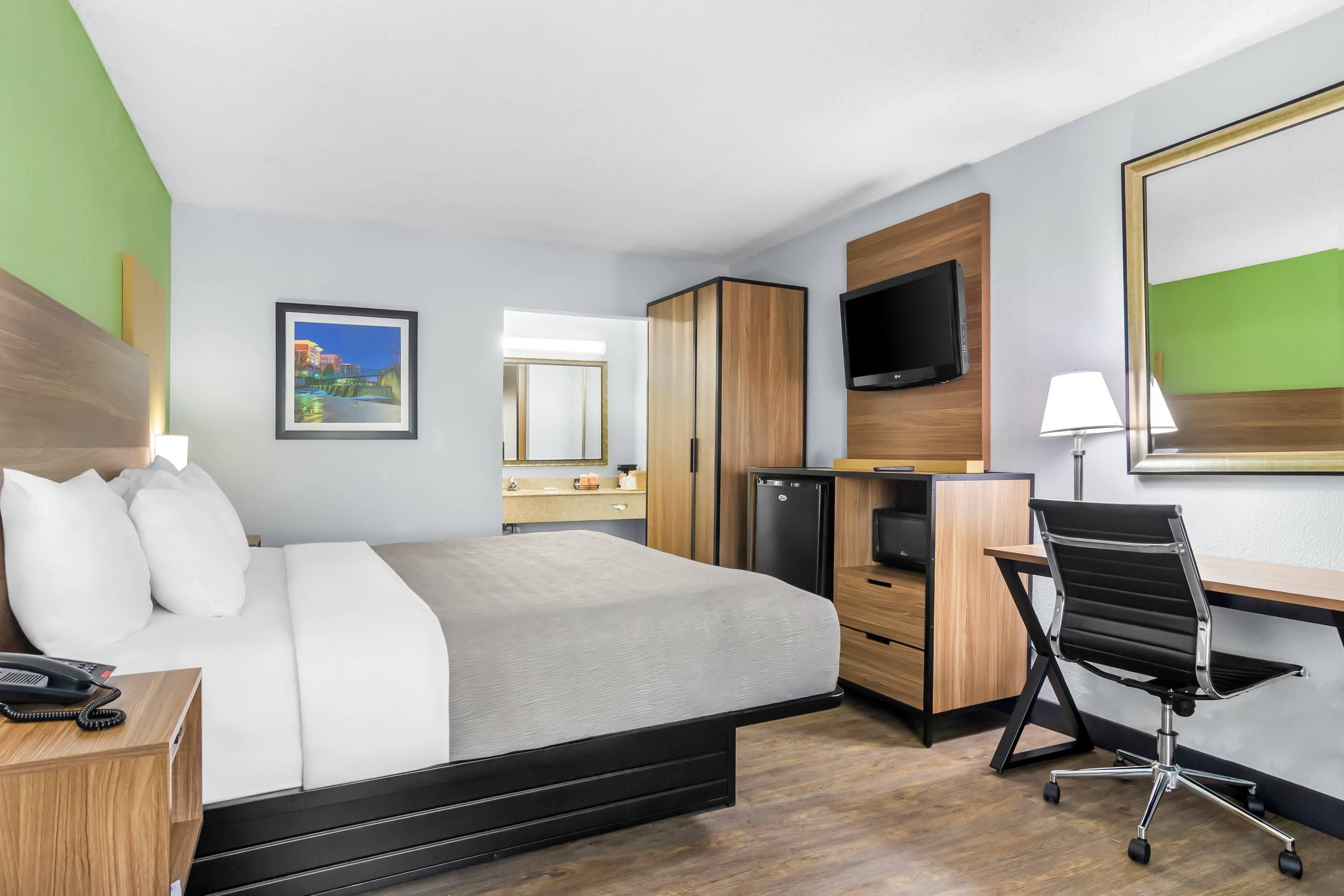 Une chambre d’hôtel équipée d’un lit, d’un bureau, d’une chaise, d’une télévision et d’un petit réfrigérateur.