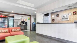 A reception area with a Coca-Cola refrigerator, a 'Quality' sign, a sofa, and a counter. - Quality Inn & Suites Greenville - Haywood Mall (Greenville)