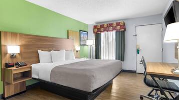 Habitación de hotel con cabecera de madera, cama con ropa blanca, escritorio con silla, teléfono y televisión.