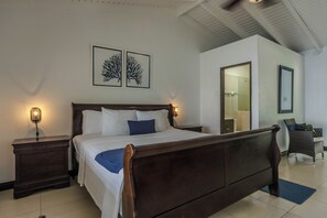 A bedroom with a wooden bed, two bedside tables with lamps, a chair, and two framed wall art pieces.