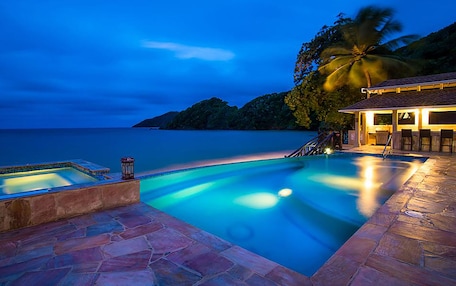 A swimming pool with a stone deck, a small hot tub, and a bar area with chairs.