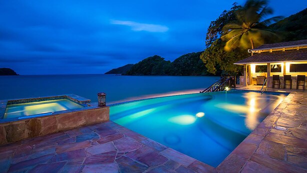 A swimming pool with a stone deck, a small hot tub, and a bar area with chairs. - Blue Waters Inn (Speyside)