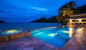 Une piscine avec une terrasse en pierre, un petit jacuzzi et un coin bar avec des chaises.