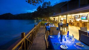 A waterfront restaurant with outdoor seating overlooking a lake, featuring a wooden deck and tables set for dining. - Blue Waters Inn (Speyside)
