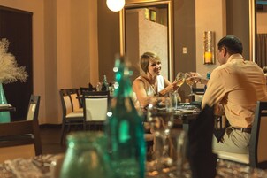 Un comedor con una mesa preparada para dos personas, un jarrón y un espejo que refleja la habitación.