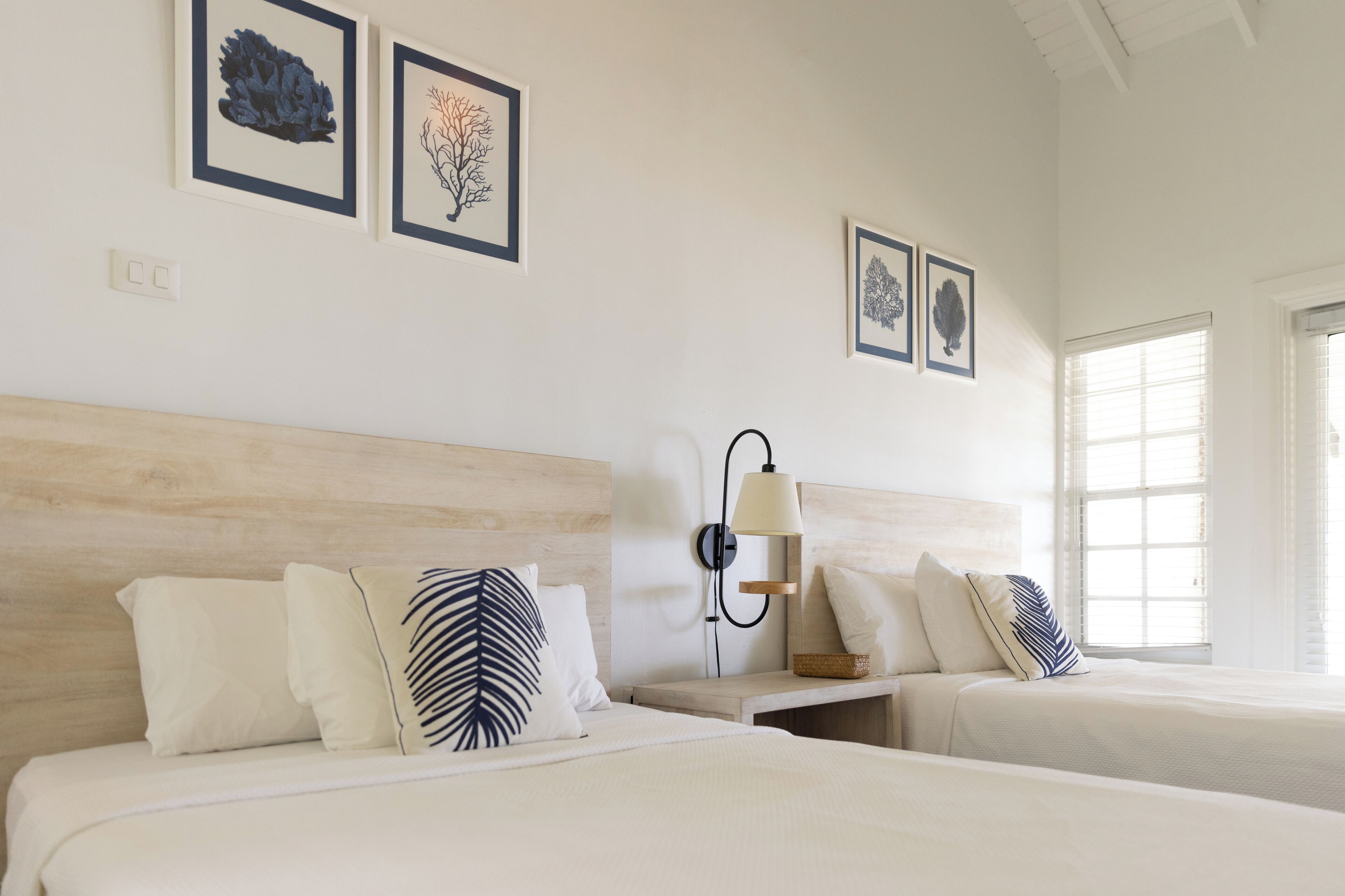 A hotel room with two beds, a nightstand, a wall-mounted lamp, and framed artwork on the wall.
