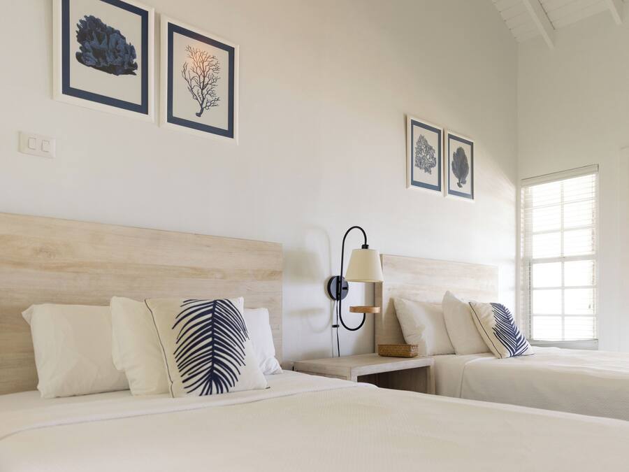 Una habitación de hotel con dos camas, una mesita de noche, una lámpara de pared y cuadros en la pared.
