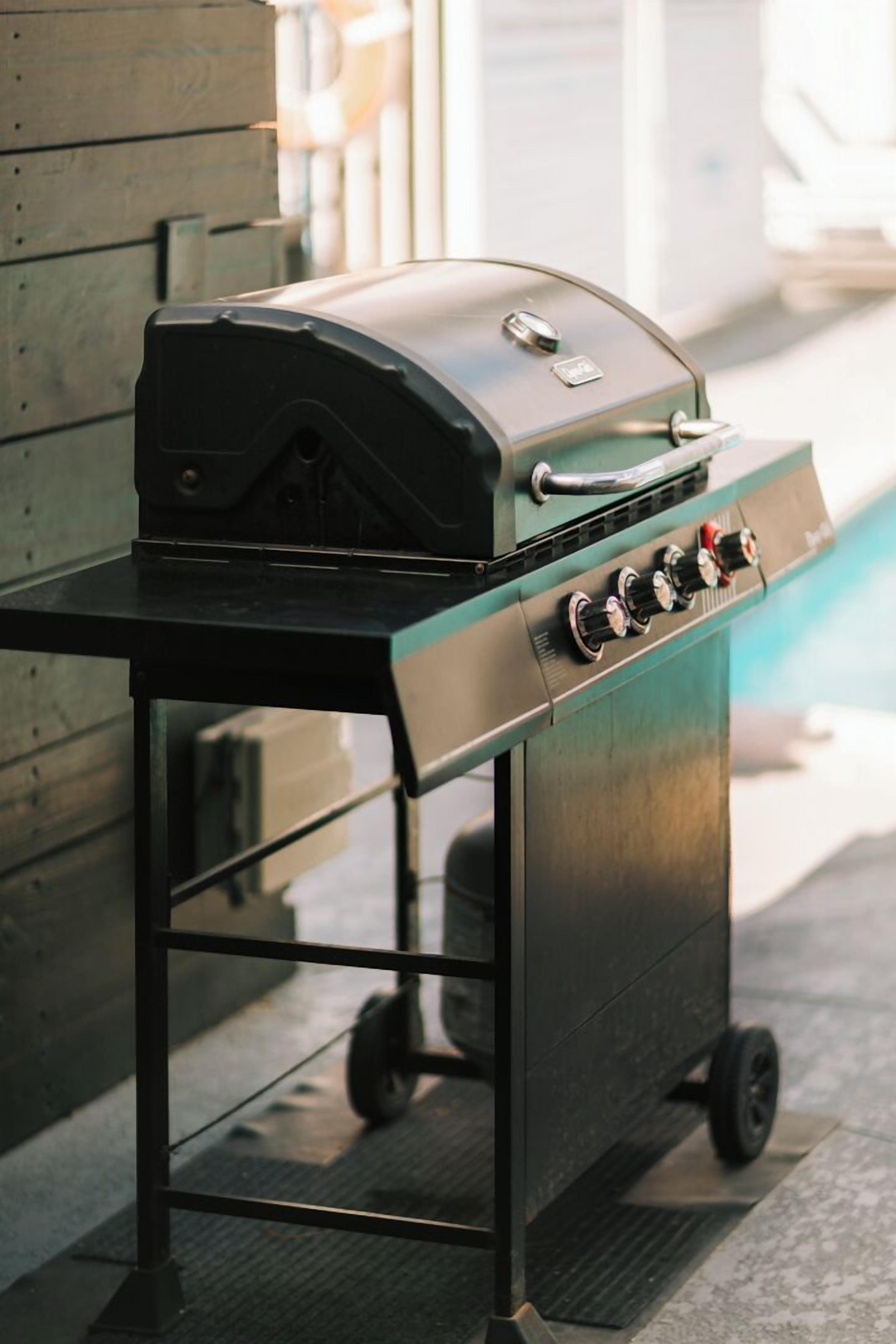 A portable grill on a metal cart with wheels, positioned outdoors.