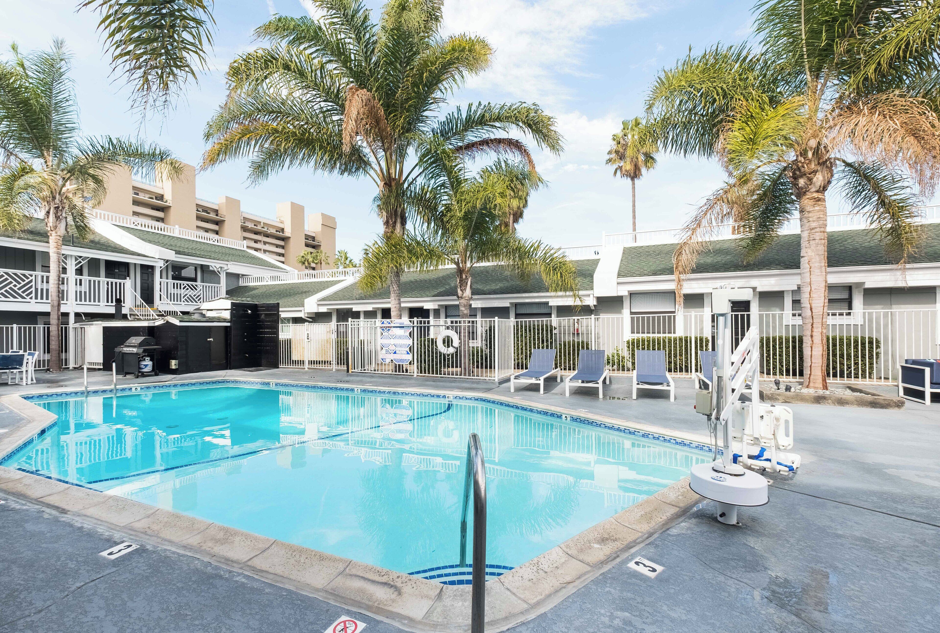 A swimming pool with lounge chairs and palm trees, surrounded by a building with balconies.