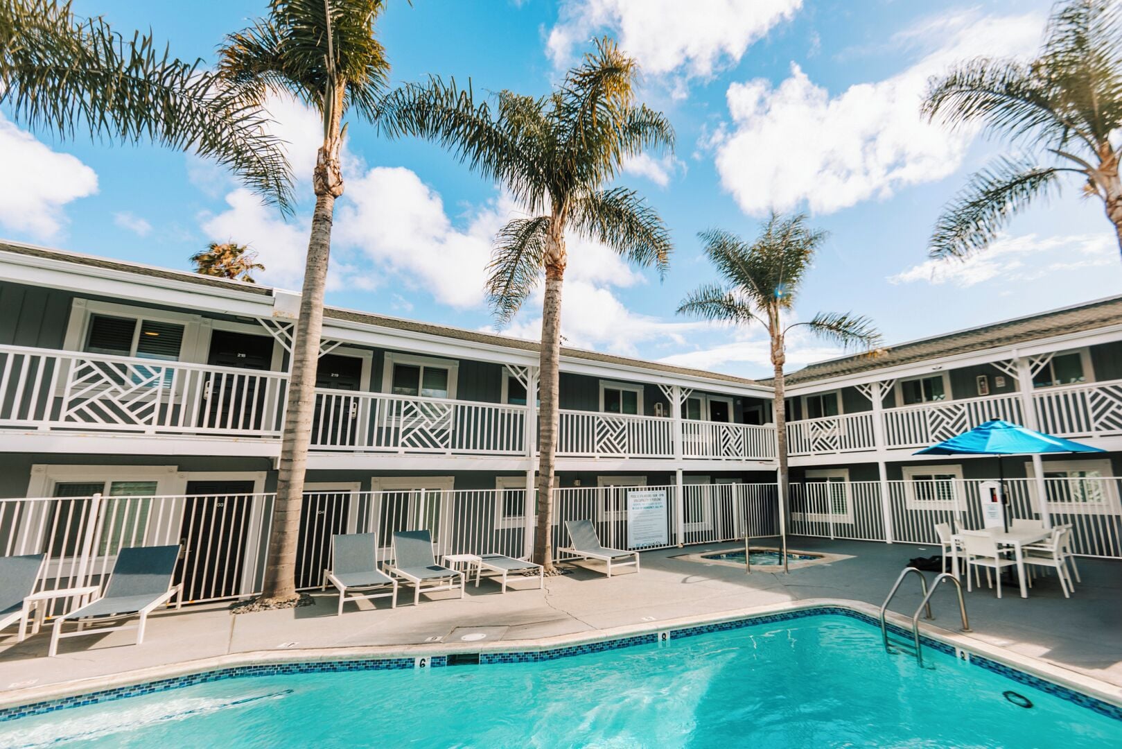 A hotel with a pool, palm trees, and a two-story building with balconies.