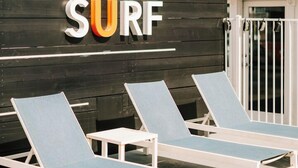 Un cartel con la palabra 'SURF' sobre una pared de madera, dos sillones blancos con cojines azules y un portón blanco.