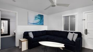 Una sala moderna con un sofá seccional azul oscuro, una mesa de centro blanca y un ventilador de techo.