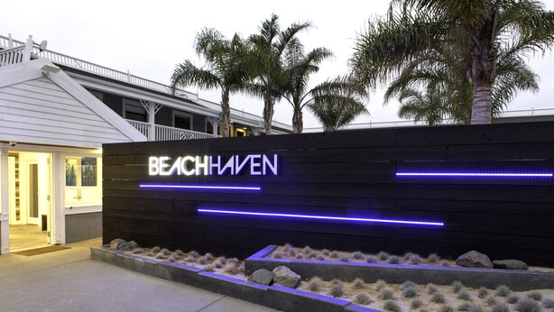 Un edificio con un letrero que dice "BEACHHAVEN" y un área ajardinada con rocas y plantas pequeñas.