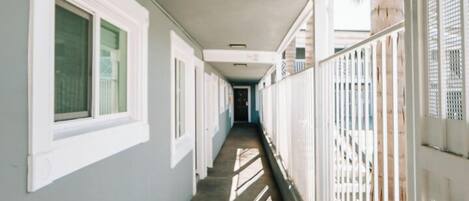 A long corridor with white-framed windows and a concrete floor, leading to a door at the end.