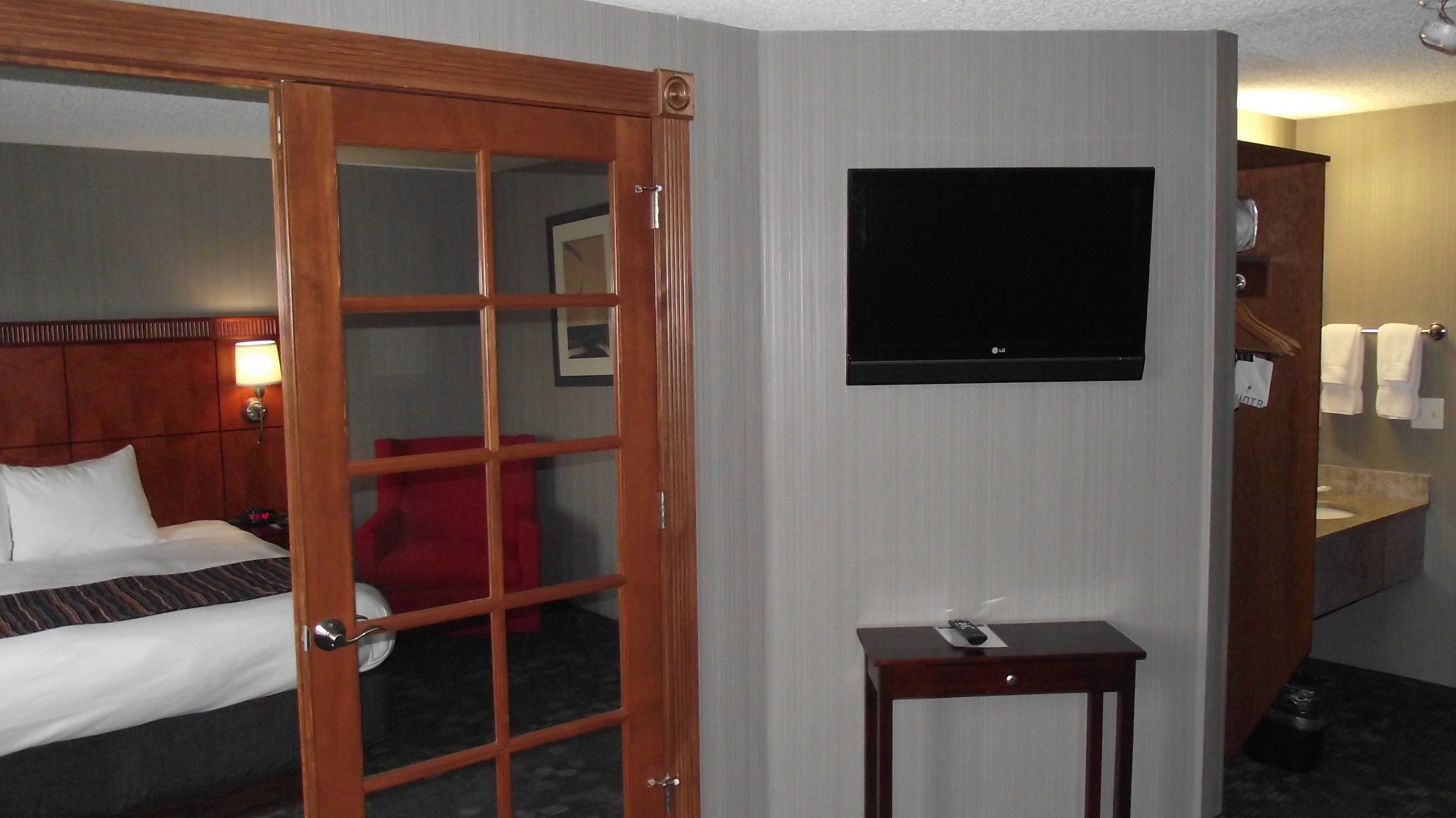Habitación de hotel con cama, televisor montado en la pared, una mesita y baño visible a través de una puerta abierta.