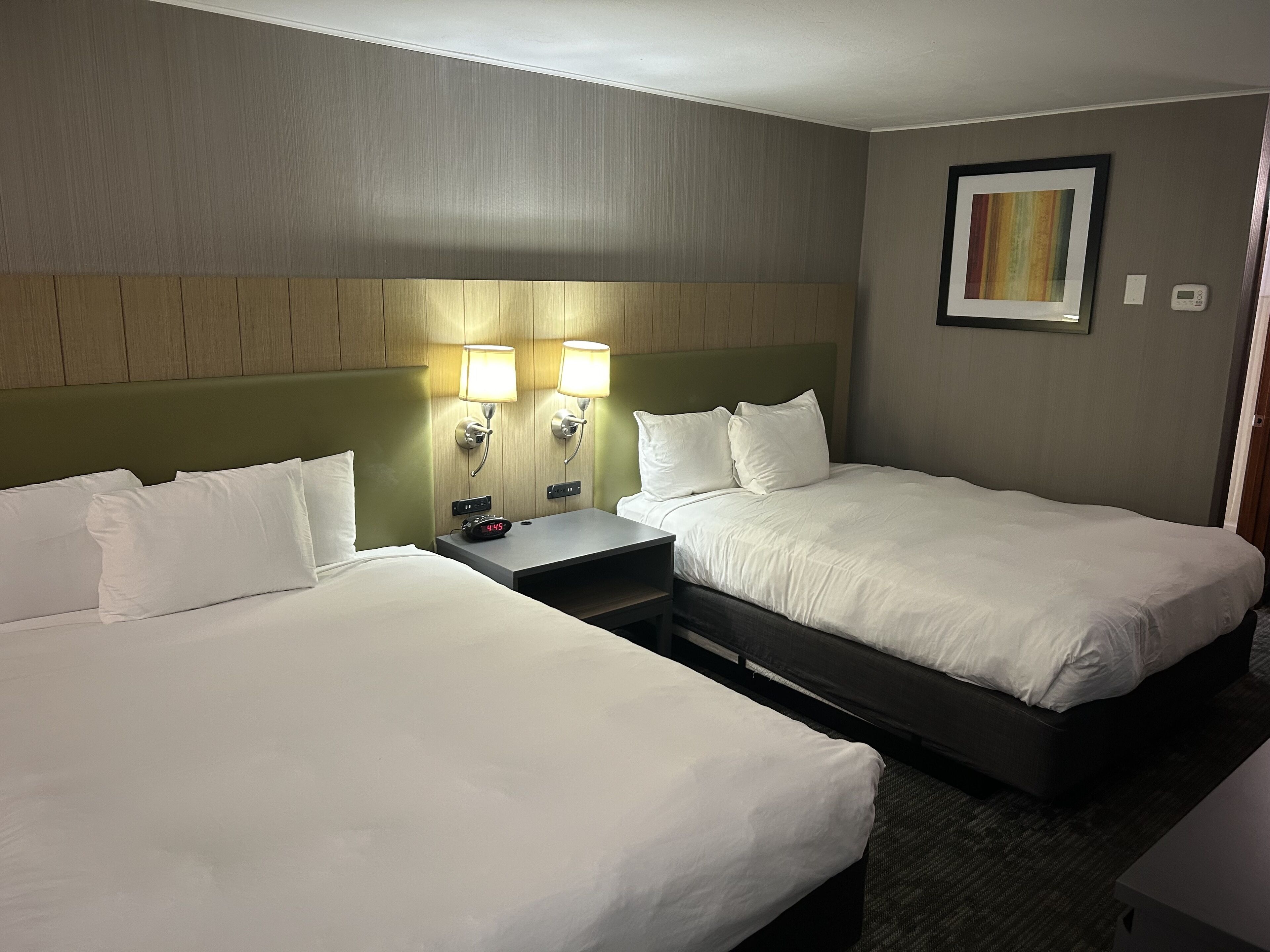 Une chambre d’hôtel avec deux lits simples, une table de chevet avec une horloge et une lampe fixée au mur.