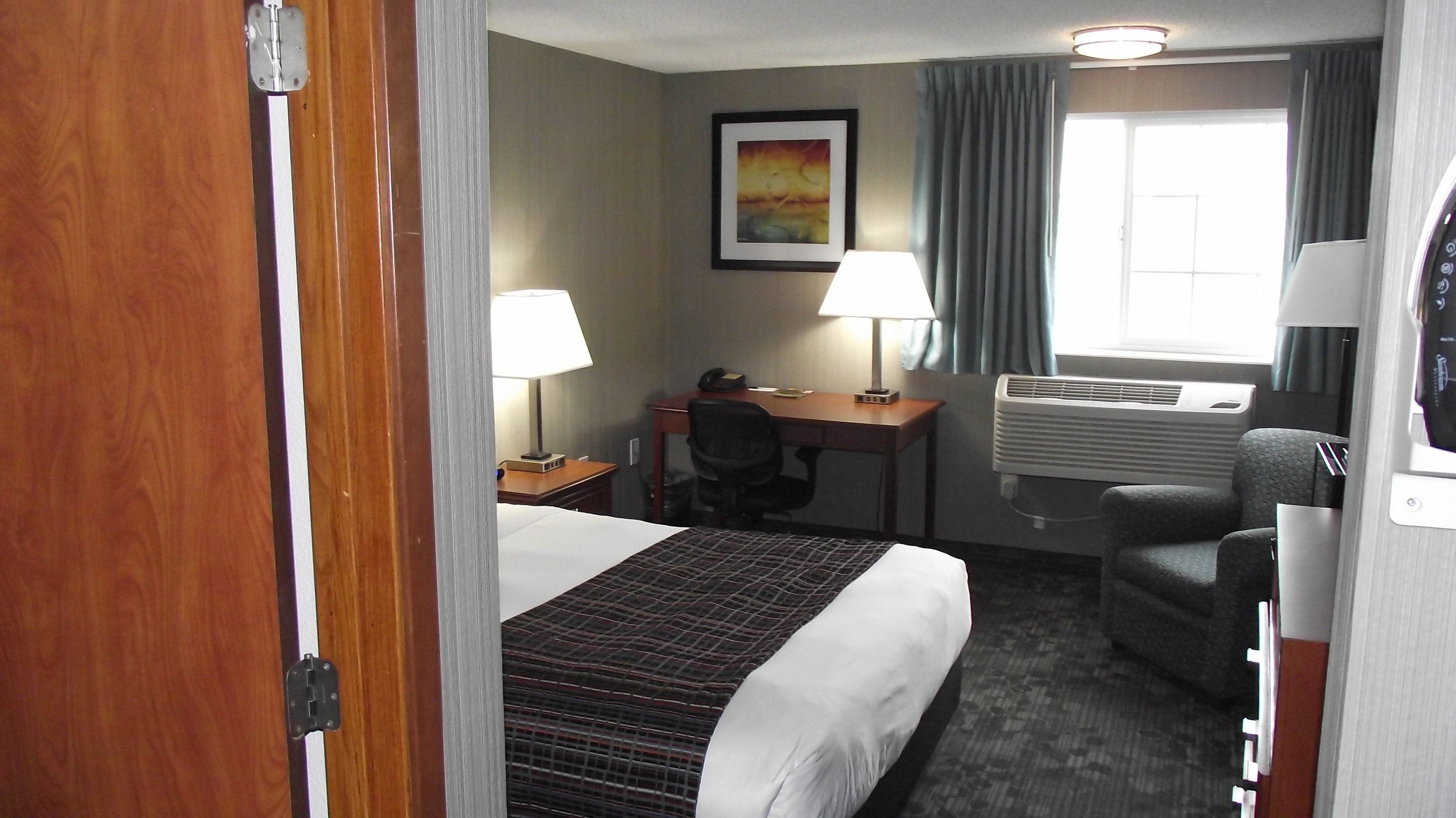 Habitación de hotel con cama, escritorio, silla, dos lámparas, aire acondicionado y ventana con cortinas.