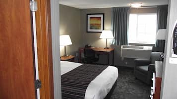 Habitación de hotel con cama, escritorio, silla, dos lámparas, aire acondicionado y ventana con cortinas.