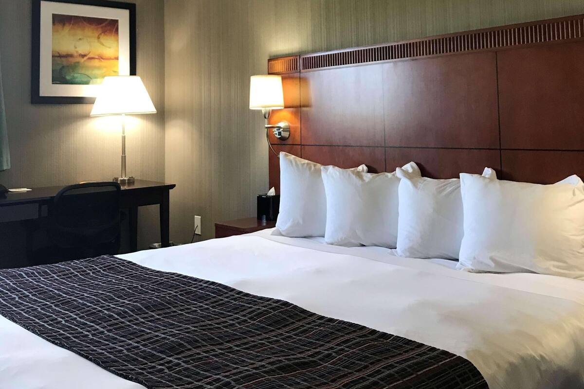 A hotel room with a large bed, two bedside lamps, a desk, and a framed picture on the wall.