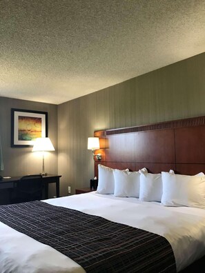 A hotel room with a large bed, two bedside lamps, a desk, and a framed picture on the wall.