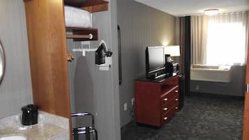 A hotel room with a bed, a TV, a desk, a lamp, and a window with curtains.