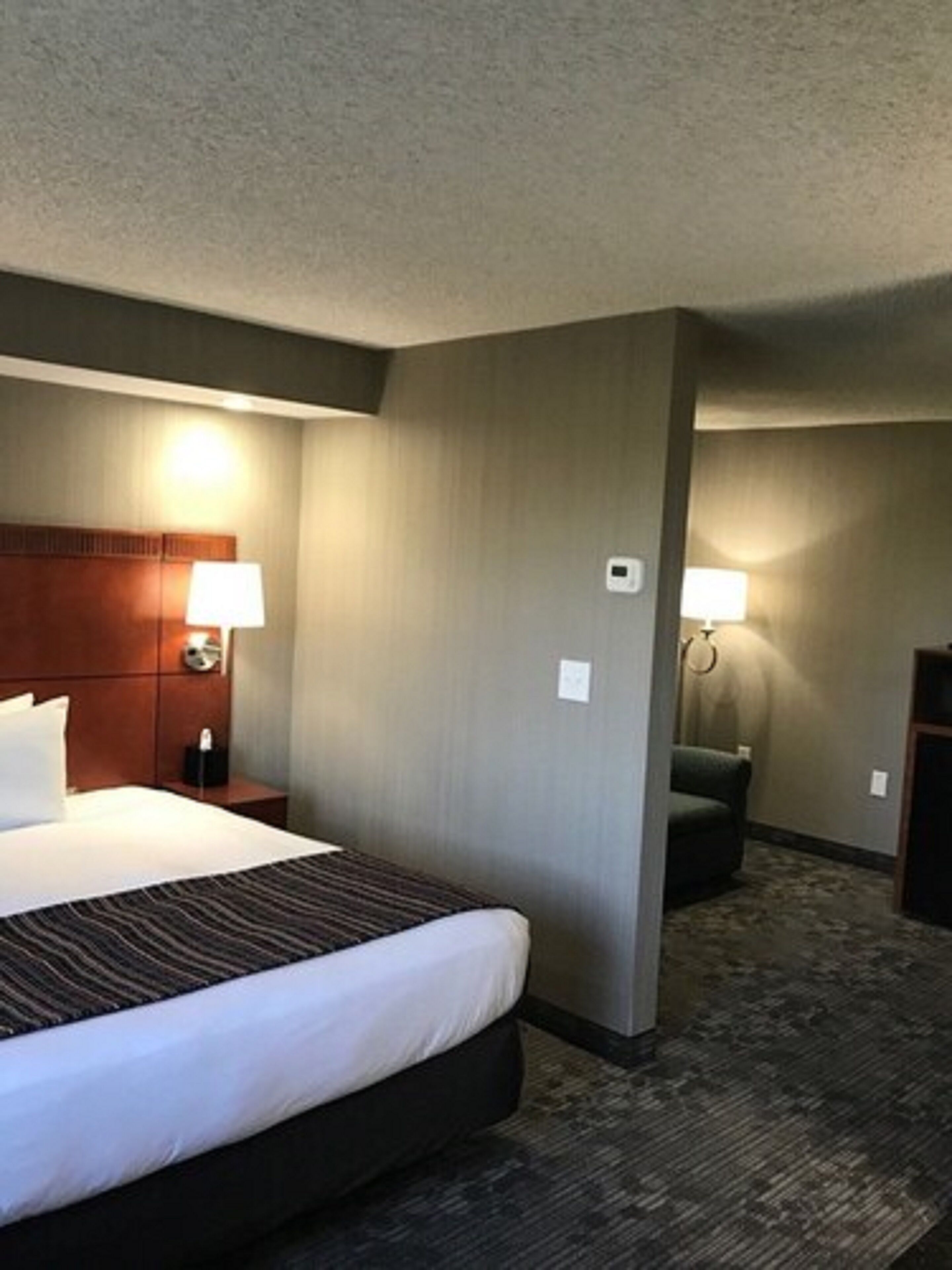 Une chambre d’hôtel avec un grand lit, une tête de lit en bois, deux lampes de chevet, un petit bureau et une chaise.