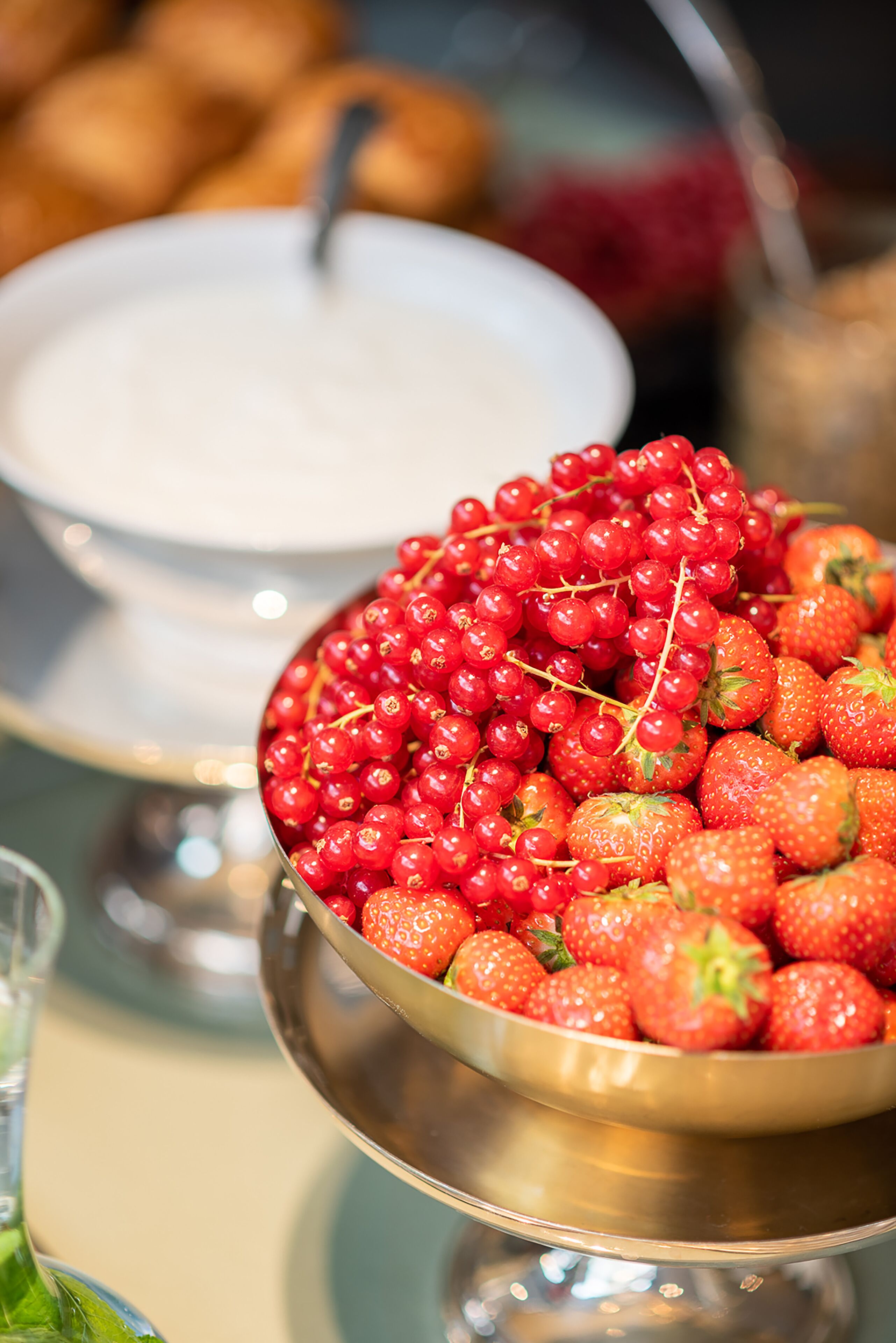 A buffet table with a bowl of strawberries and red currants, a white bowl with a spoon, and a glass of water.