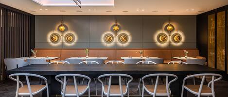 A modern dining area with a long table and white chairs, recessed lighting, and a skylight above.