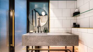 A modern bathroom with a granite sink, a round mirror, and a glass shelf.