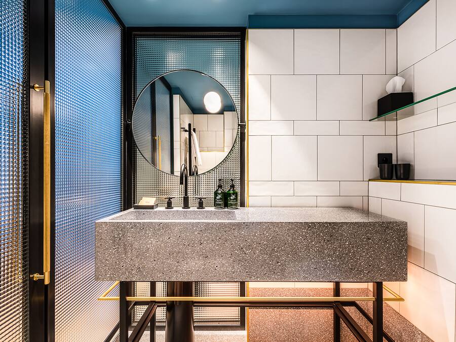 A modern bathroom with a granite sink, a round mirror, and a glass shelf.