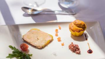 Un plat composé d’un morceau de viande, d’une petite tomate et d’un muffin, le tout présenté sur une assiette blanche.