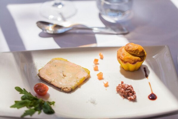 Un plato con un trozo de carne, un tomate pequeño y un muffin sobre un plato blanco.