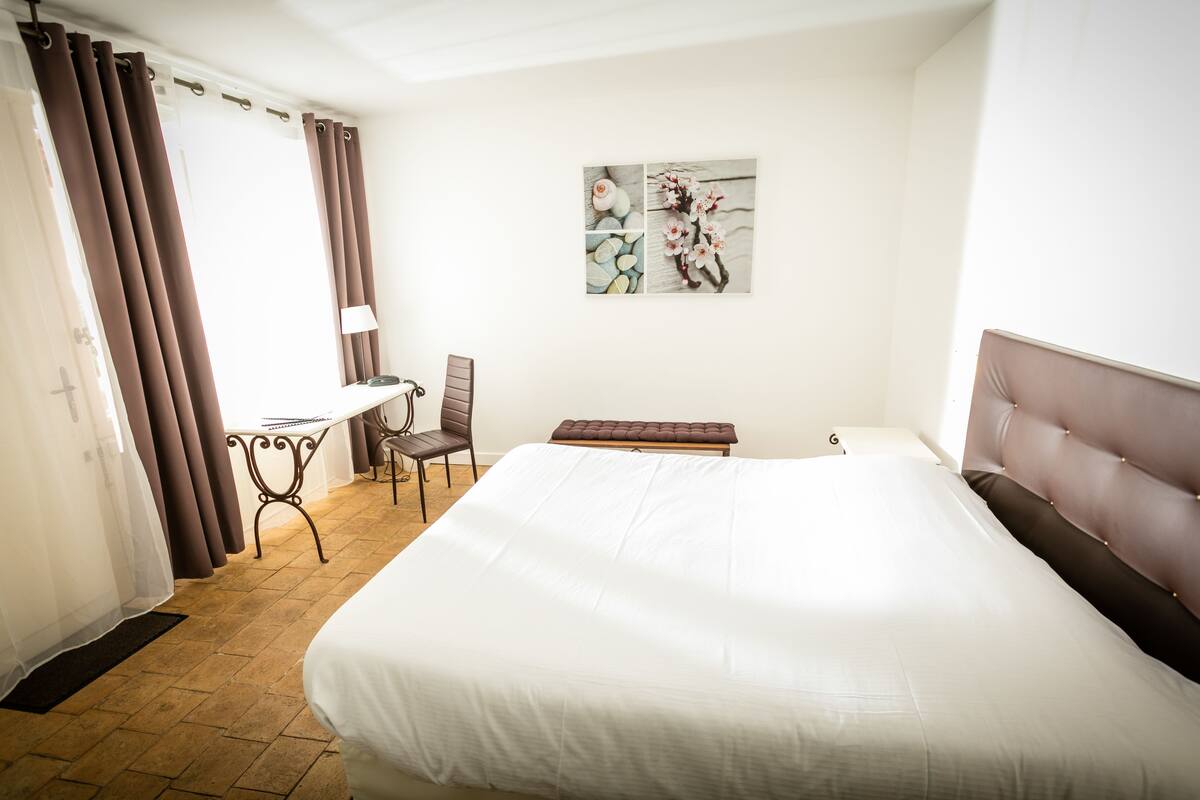 Une chambre d’hôtel avec un grand lit, un bureau avec une chaise, une petite table et un banc.