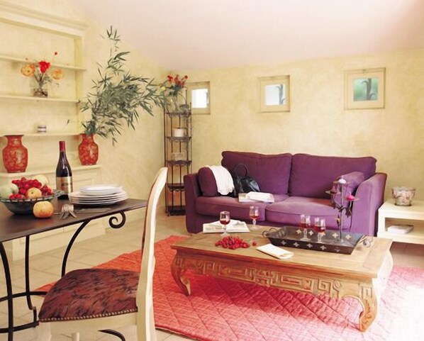 Un salon avec un canapé violet, une table basse et un coin repas avec une table dressée pour deux personnes.