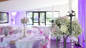 Un salón de recepciones de bodas con mesas redondas, manteles blancos y centros de mesa florales.