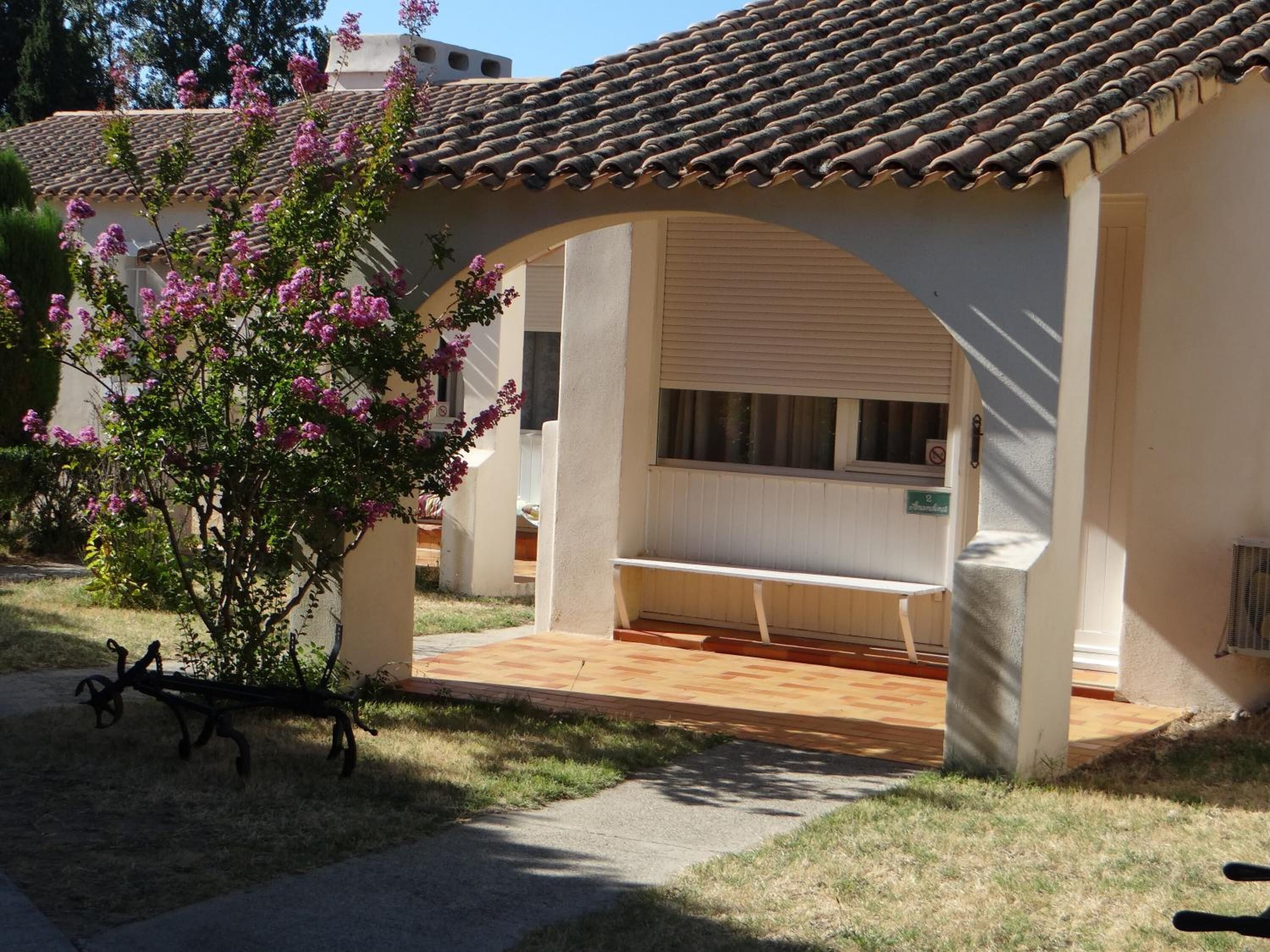 A covered outdoor seating area with a bench, a small table, and a potted plant.
